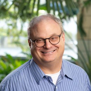 man with glasses blue shirt and plants backdrop
