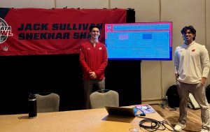 Two men posing in front of TV screen