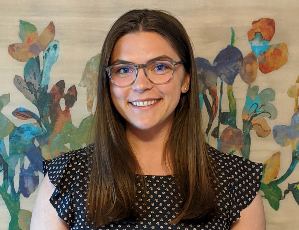 Dana is brunette, wearing a polka dotted sleeveless top and glasses. 
